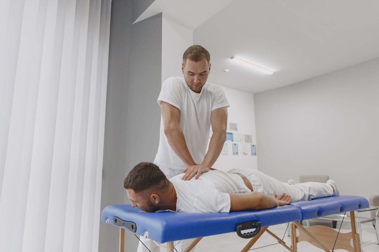 A professional masseur giving a back massage to a client on a massage table in a tranquil room.